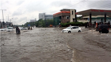 Pendler fahren in Lahore eine überschwemmte Straße entlang.