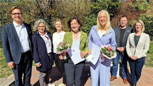 Schulsekretärin arbeitet seit 20 Jahren für den Landkreis Wesermarsch Fünf Frauen und zwei Männer stehen in einer Reihe nebeneinander. Die beiden Frauen in der Mitte halten je einen Blumenstrauß und eine Urkunde in den Händen.