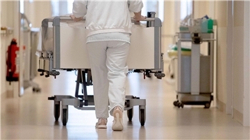 Eine Krankenpflegerin schiebt ein Krankenbett durch einen Flur. 