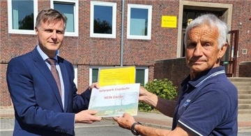 Zwei Männer stehen vor dem Nordenhamer Rathaus. Der rechte Mann überreicht eine Mappe mit Unterschriftenlisten. 1400 haben unterschrieben. Sie wollen keinen Solarpark in Abbehausen.