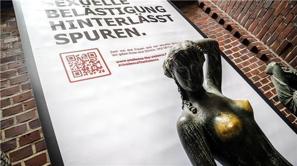 Plakat mit der Aufschrift „Sexuelle Belästigung hinterlässt Spuren“ hinter der Bronzeskulptur „Jugend“ von Bernhard Hoetger in Bremen.