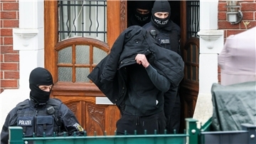 Polizeibeamte führen einen Tatverdächtigen aus einem durchsuchten Haus. 