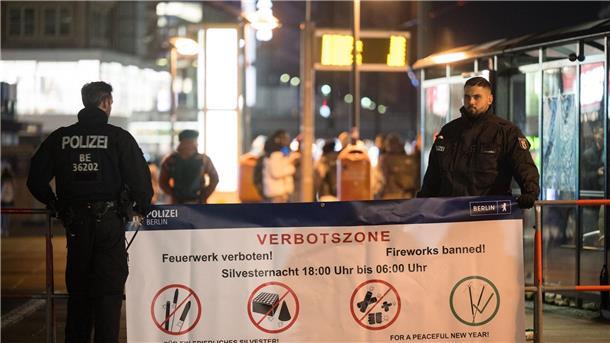 Polizeibeamte stehen an einem Plakat, das auf die Böllerverbotszone am Berliner Alexanderplatz hinweist.