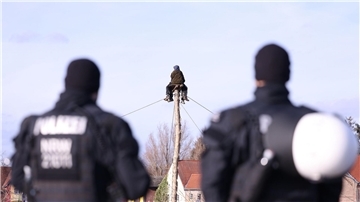 Polizisten beobachten zwei Klimaschutzaktivisten die auf einem Monopod am Rand des Braunkohledorfes Lützerath sitzen.