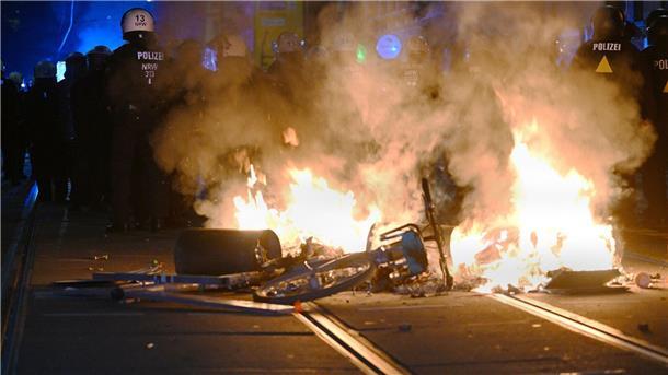 Polizisten hinter einer brennenden Barrikade.