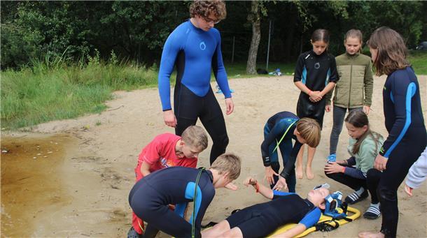 Proband Felix Staack wird aus dem See gerettet und von einigen Kindern versorgt. Betreuer Bjarne Dreyer beobachtet den Einsatz und gibt Ratschläge.