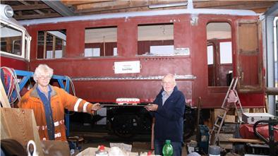 Professor Jochen Ewald (links) und Bahn-Enthusiast Rolf Gerdes vor dem rund 95 Jahre alten Triebwagen der Butjadinger Bahn. In der Hand halten beide ein Modell des Wagens in der Original-Lackierung, die der Zug zum Schluss auch wieder erhalten soll.