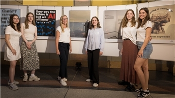 Sechs Frauen stehen in einer Ausstellung vor gestalteten Plakaten zum Thema „Campus der Zukunft“. Zu sehen sind u. a. Motive mit VR-Brille, Wegweisern und einem Schriftplakat zu Künstlicher Intelligenz.