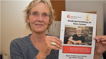 Projekt-Betreuerin Christine Sassen-Schreiber zeigt das Plakat der erfolgreich verlaufenen Auftaktveranstaltung, eines Mundorgel-Nachmittags im September mit Klaus Zurhold