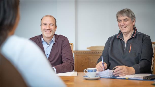 Ein Projektorganisator und ein Dozent sitzen an einem Tisch.