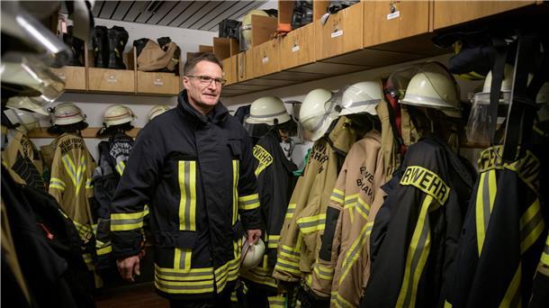 „Seute Deern“: Feuerwehr-Einsatzleiter erzählt von seinen Einsätzen Ein Feuerwehrmann steht in voller Montur in der Umkleidekabine zwischen Feuerwehranzügen.