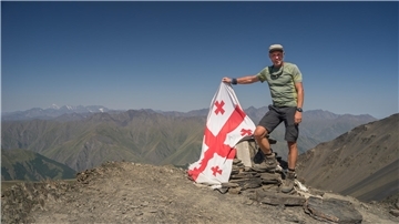 Mann mit Flagge auf einem Berg. Ralf Schwan hat den Kaukasus bereist und bringt von dort viele Bilder zu seinem Vortrag in der Rodenkircher Markthalle.