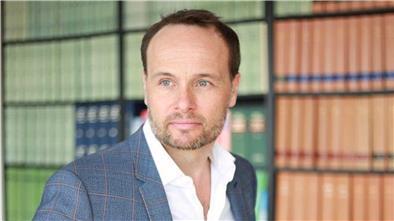 Rechtsanwalt Wolfgang Wittmann steht vor einem Bücherregal.