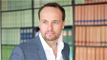 Rechtsanwalt Wolfgang Wittmann steht vor einem Bücherregal.