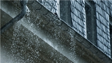 Regenwasser fließt während eines Unwetters an einer überfüllten Regenrinne hinunter.