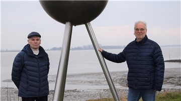 Zwei ältere Herren stehen neben dem Sonnen-Modell des Planetenwegs in Nordenham. 