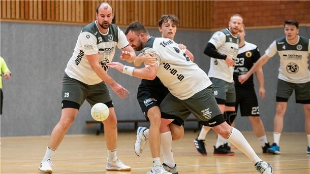 Ein Mann in einem weißen Trikot und einem kleinen weißen Ball wird von einem anderen Mann festgehalten und drei andere Männer schauen zu.