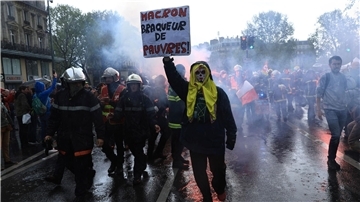 Rettungskräfte und ein Demonstrant mit einem Plakat mit der Aufschrift „Macron, Räuber der Armen“ marschieren während einer Demonstration anlässlich des Tages der Arbeit in Paris.