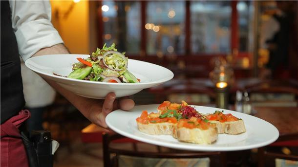Ein Kellner trägt zwei Teller, auf denen Salat und Bruschetta angerichtet sind.