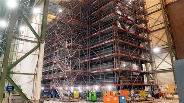 Großes Schleusentor im Rohbau, eingerüstet in einer Produktionshalle bei Stahlbau Nord in Bremerhaven; rund 42 Meter langes Stahlbauwerk mit Arbeitsgerüsten und Baumaschinen davor.
