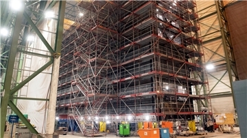 Großes Schleusentor im Rohbau, eingerüstet in einer Produktionshalle bei Stahlbau Nord in Bremerhaven; rund 42 Meter langes Stahlbauwerk mit Arbeitsgerüsten und Baumaschinen davor.
