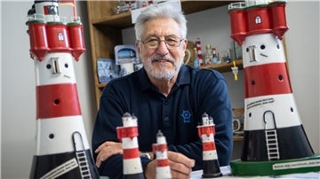 Rolf Pilz, Vorsitzender vom Förderverein Leuchtturm Roter Sand, sitzt zwischen Modellen des Leuchtturms in seinem Büro.