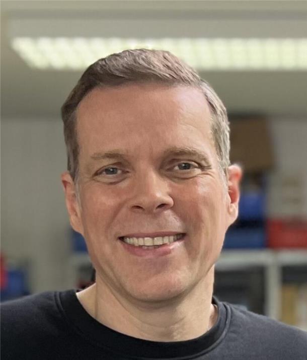 Ein Mann, der lächelt. Er trägt kurze, braune Haare.