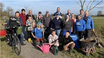 Gruppe von Menschen mit Spaten, Schubkarren und Gießkannen