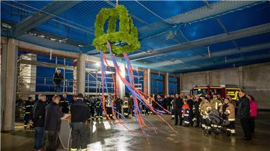 Ein Richtkranz hängt an der noch offenen Decke der Fahrzeughalle, die Gäste in Feuerwehrkleidung und Zivil lauschen den Grußworten. 