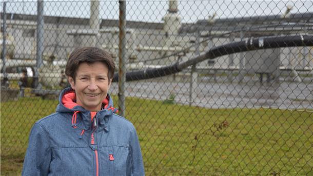 Eine Frau steht vor einem Maschendrahtzaun, der eine Gasförderstation einzäunt.