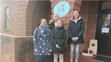 Vier Frauen stehen vor dem Schild des Kindergartens in Cappel. Darauf sind zwei Kinder zu sehen und es steht geschrieben: "De lütte Kinnerstuv".