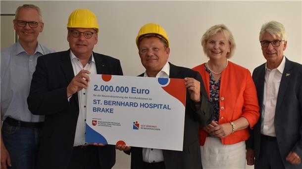 Vier Männer und eine Frau stehen nebeneinander, zwei Männer halten einen symbolischen Scheck.