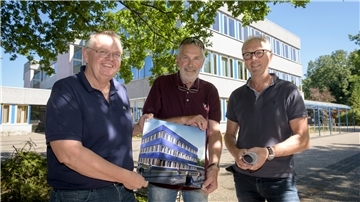 Drei Vertreter der Stadt Bremerhaven - Kämmerer torsten Neuhoff, Sportausschuss-Sprecher Detlef Müller und Holger Schneeberg von Seestadt-Immobilien - stehen vor der alten Fassade der Schule am Leher Markt und zeigen die Zeichnung, wie die neue blaue Energiespar-Fassade demnächst aussehen wird.