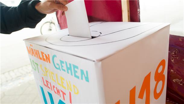 Eine Wahlurne, in der ein Stimmzettel eingeworfen wird.