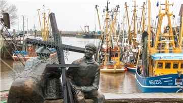 Schwarze Holzkreuze lehnen an der Bronezeskulptur „Alt- und Jungfischer“ im Hafen in Neuharlingersiel. Das Fischen mit Grundschleppnetzen steht in der Kritik.