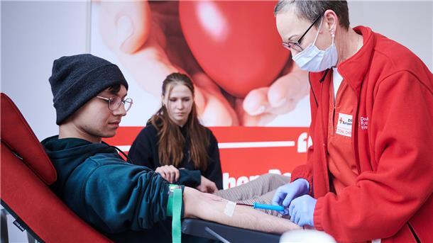 Ein junger Mann spendet Blut. Eine DRK-Mitarbeiterin setzt die Kanüle.