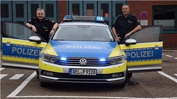 Der Polizeihauptkommissar Andreas Bathke und Leiter vom Einsatz- und Streifendienst Matthias Ahlers stehen an geöffneten Türen ihres Einsatzfahrzeuges. 