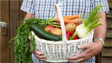 Ein Mann hält einen Korb mit Obst und Gemüse in der Hand.