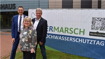 Zwei Männer und eine Frau stehen vor einem Transparent.