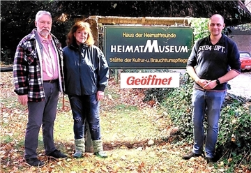 Zwei Männer und eine Frau stehen neben einem Schild mit der Aufschrift Heimatmuseum.