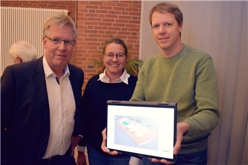 Zwei Männer und eine Frau zeigen etwas auf einem Laptop