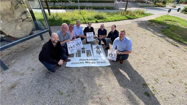 8 lächelnde Leute sitzen in der Hocke mit Plakaten „Rücksicht macht Wege breit“