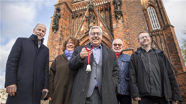 Große Kirche Bremerhaven: Sie wollen den Klang unserer Stadt retten Vier Männer und eine Frau stehen vor der Großen Kirche in Bremerhaven. Ein Mann hält ein kleines weißes Glöckchen in der Hand.