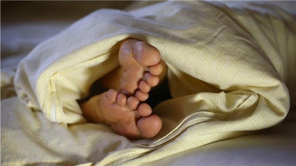 Wie guter Schlaf zu mehr Erfolg im Leben führt Zwei Füße schauen aus einer Decke heraus.