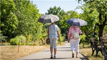 Zwei Frauen gehen unter Schirmen und in sommerlicher Kleidung spazieren.