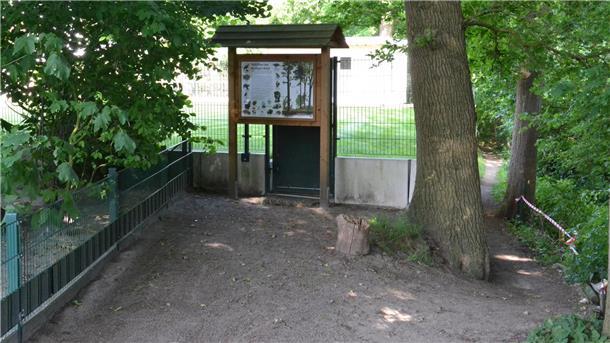 Spaziergänger aus Richtung Offensen biegen vor dem Grundstückszaun und der Schautafel rechts ab auf den Trampelpfad, um den Weg fortsetzen zu können.