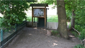 Spaziergänger aus Richtung Offensen biegen vor dem Grundstückszaun und der Schautafel rechts ab auf den Trampelpfad, um den Weg fortsetzen zu können.