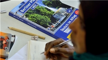 Das Lehrbuch "Deutsch im Alltag" liegt in einem Deutschkurs für Flüchtlinge vor einer jungen Frau auf der Schulbank.