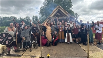 Menschen im Wikinger-Outfit vor einer Wikinger-Hütte.