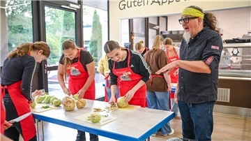 Jugendliche schneiden Gemüse, während ein Mann Anweisungen gibt.